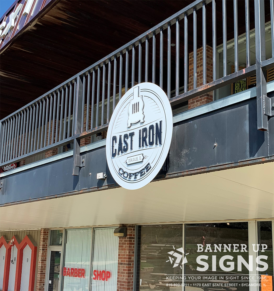 A round cut aluminum sign with dimensional graphics showcases a businesses logo over their entrance.