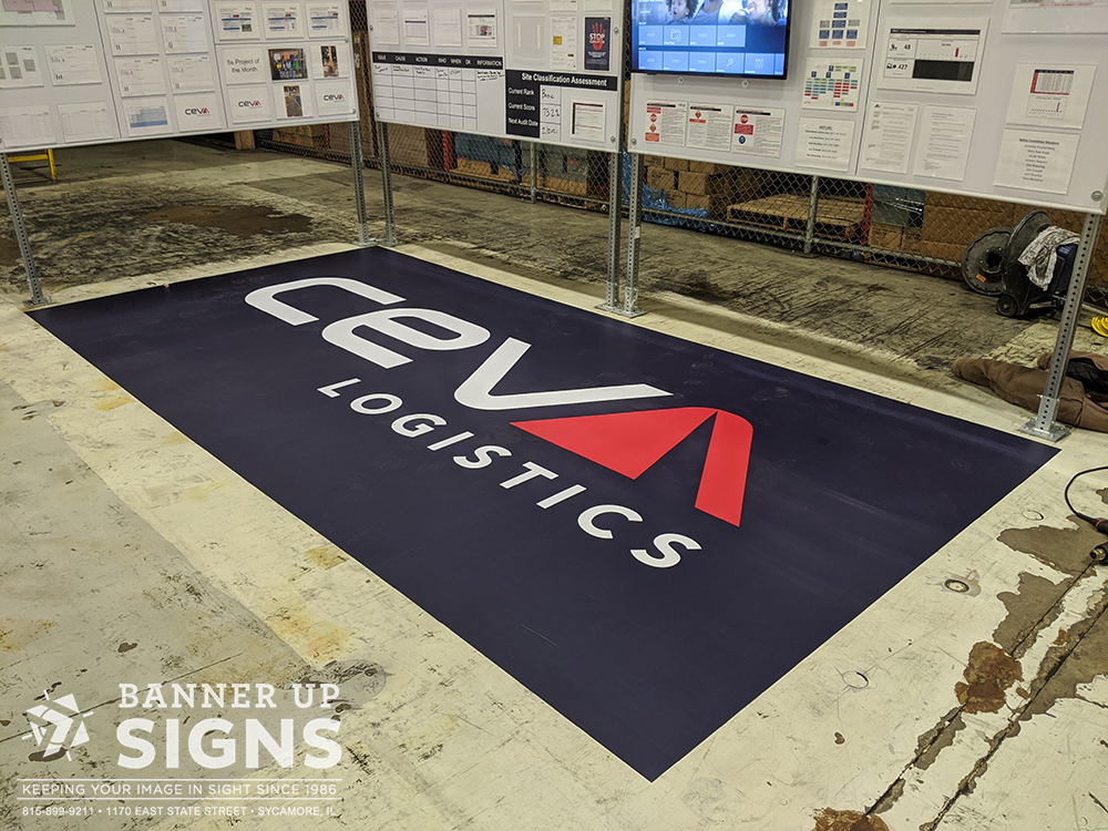 A large decal of a company's logo is installed on the floor next to a warehouse display.