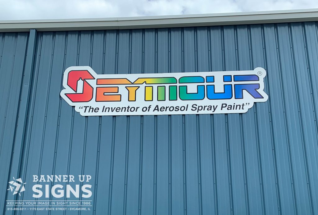 A cut to shape flat panel with colorful graphics on the side of a building was created and installed for Seymour by Banner Up Signs.