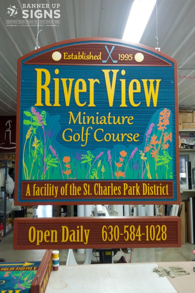 A hanging HDU sign for St. Charles Park District's mini-golf location informs patrons of the daily openings and contact information.