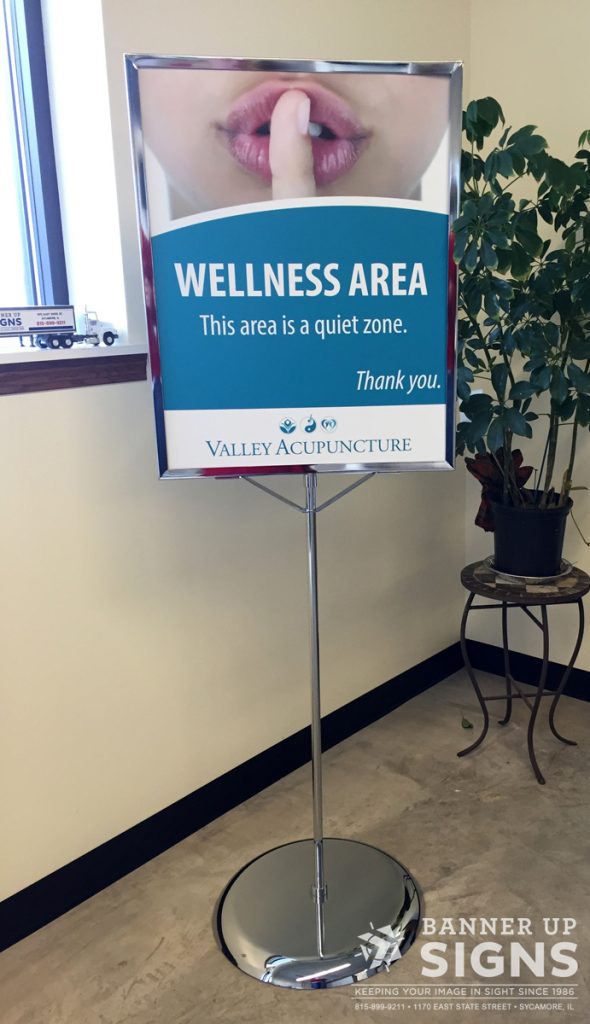 A silver floor stand displays a poster.