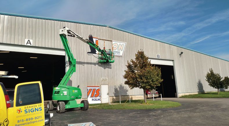 Using a cherry picker, the Banner Up Signs team installs an exterior sign on a warehouse.